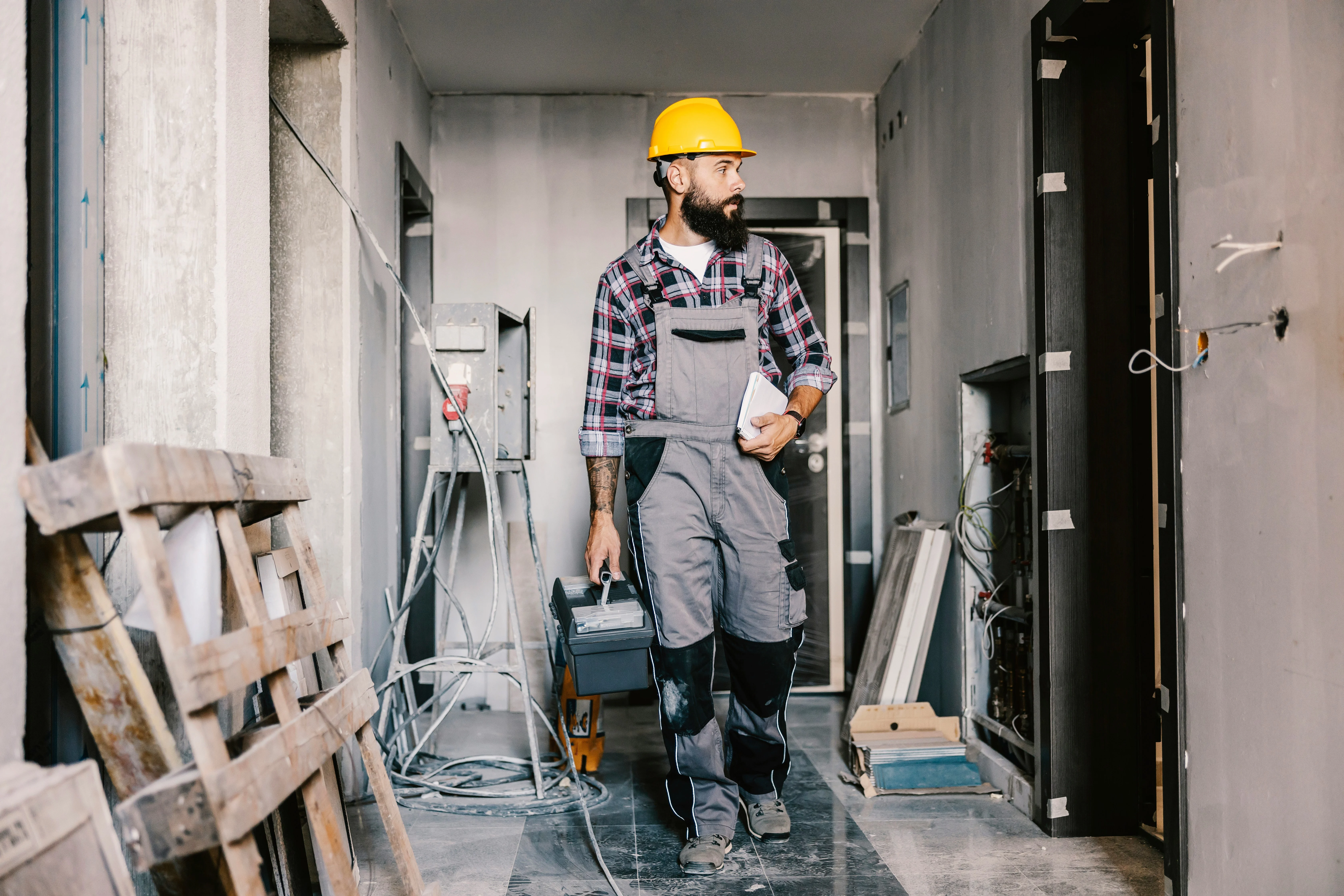 Hard-hatted plumber carrying a toolbox on a renovation job site