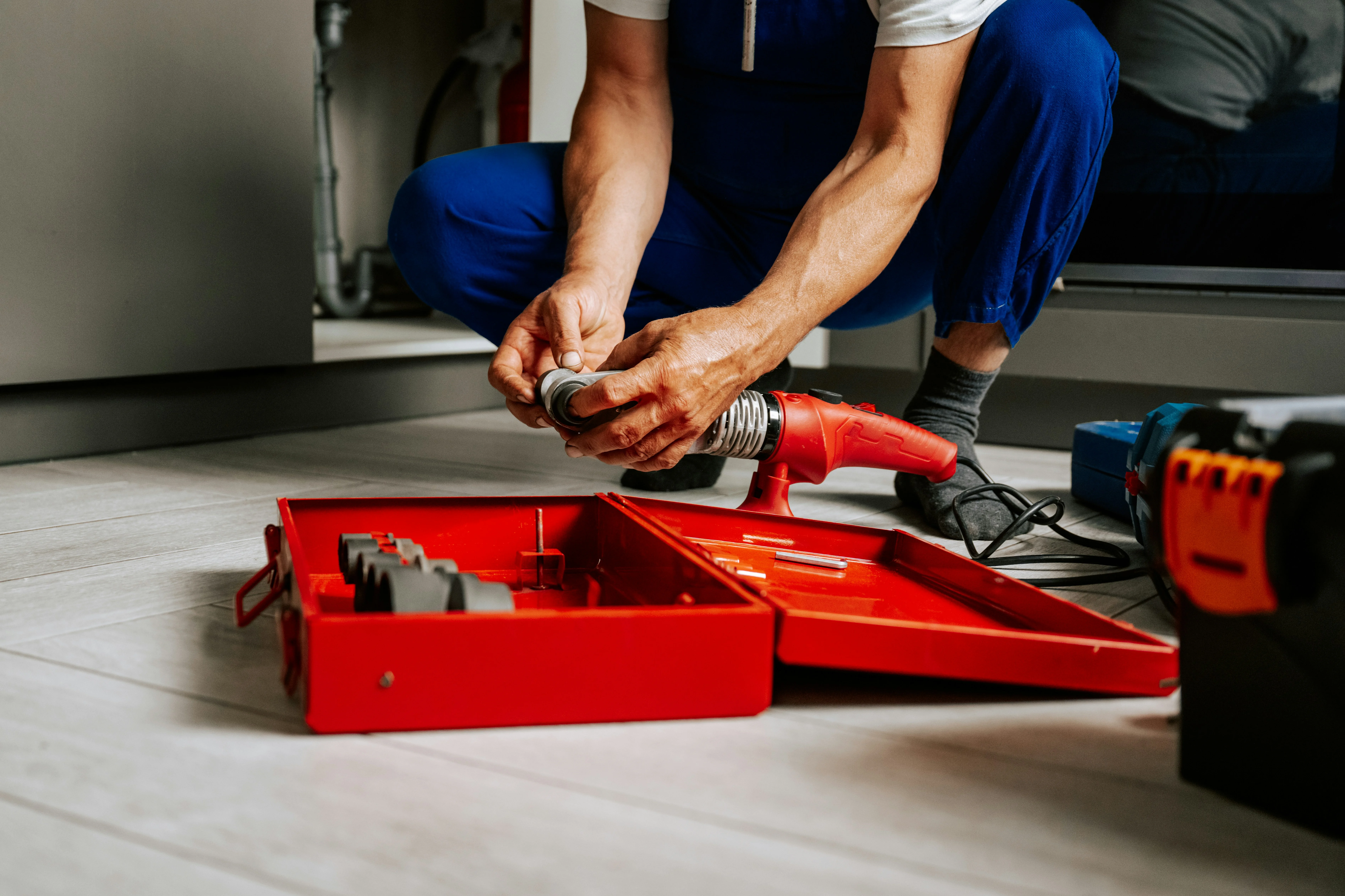 Plumber working near a sink with an open red toolbox