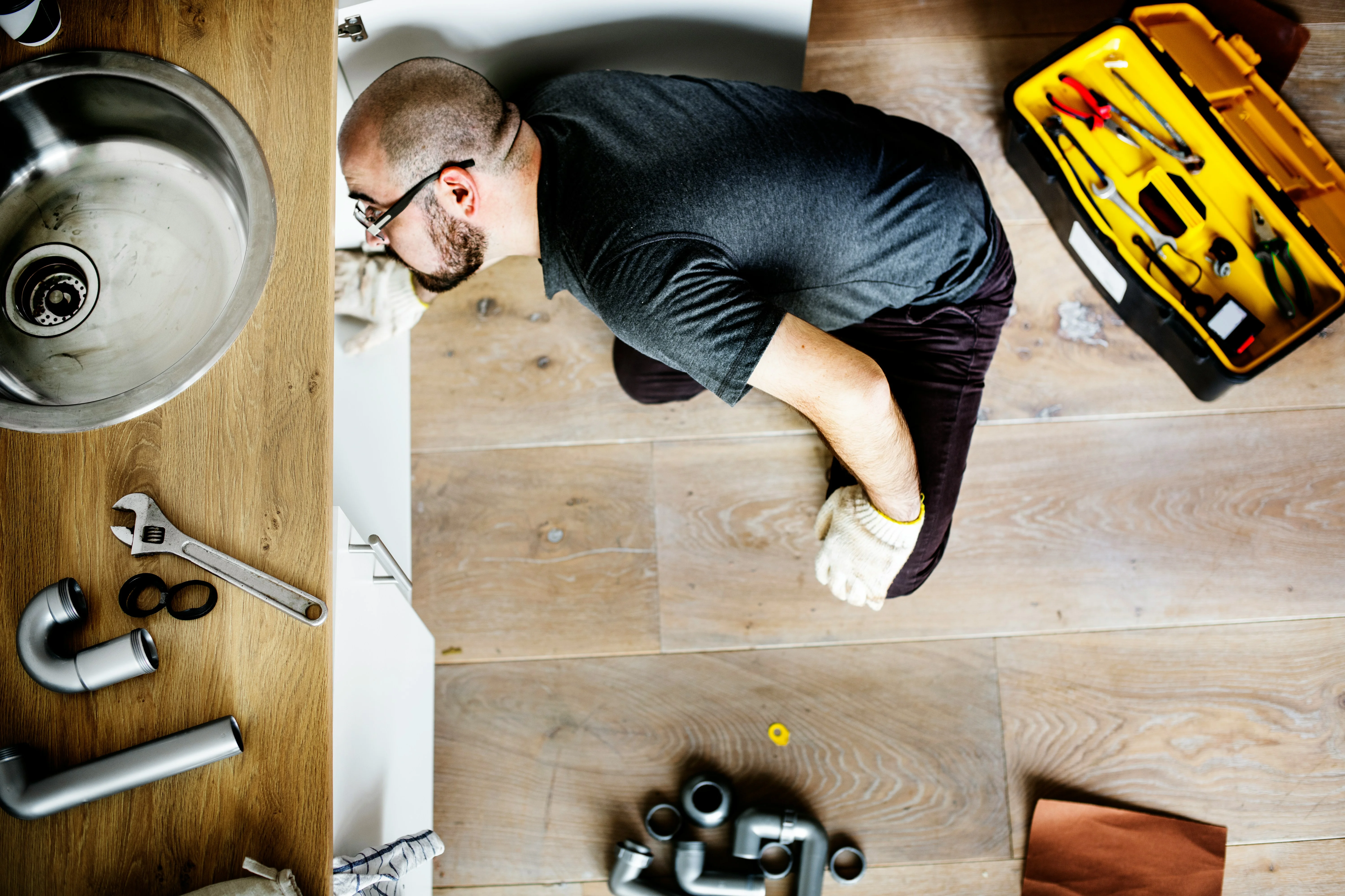 Plumber repairing a kitchen sink from above with tools and toolbox